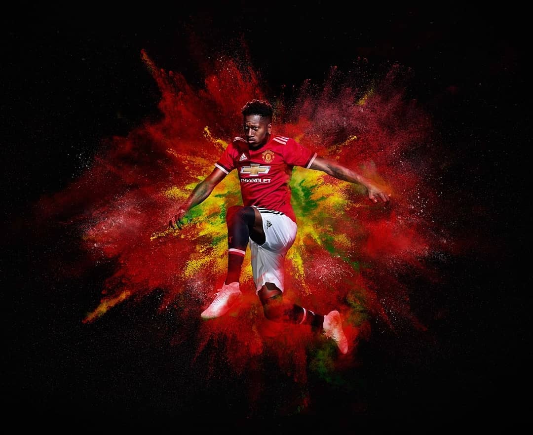 Athlete jumps against black background with explosive red and yellow powder effect, wearing a red jersey and matching athletic shoes.