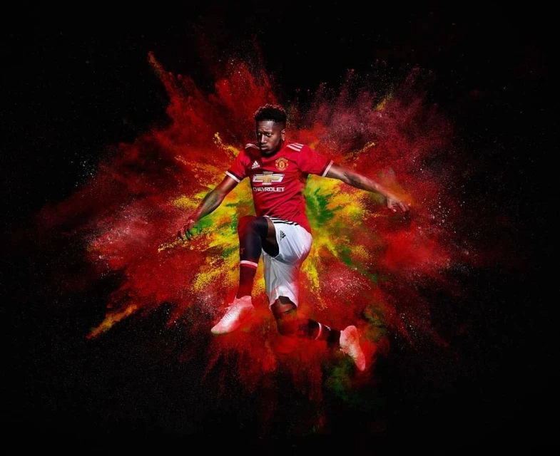 Athlete jumps against black background with explosive red and yellow powder effect, wearing a red jersey and matching athletic shoes.