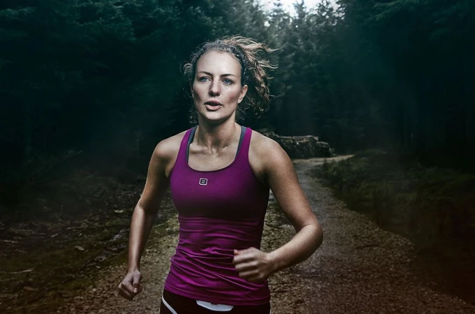 Woman running along a dirt forest path wearing a magenta athletic tank top, captured by photographer Guy Farrow.
