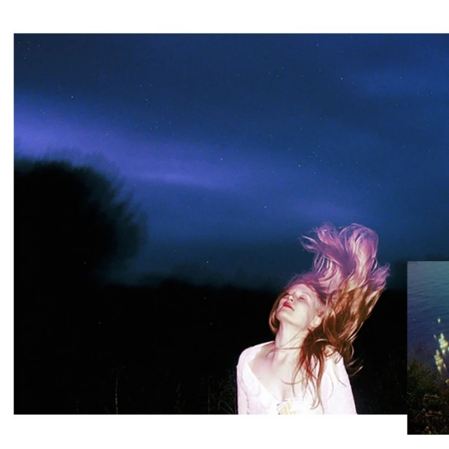 Young woman tossing hair against a backdrop of dark forest and vibrant blue night sky filled with stars, creating a dreamy scene.