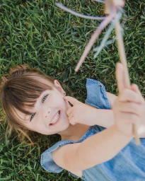 Young child in a blue dress lying on green grass holding a ribbon wand