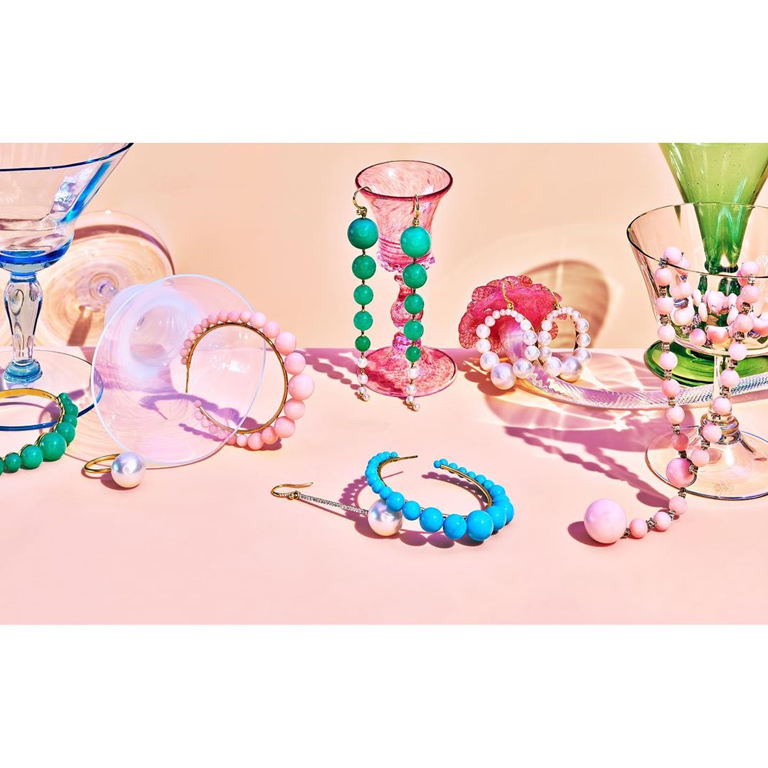 Still life with beaded jewelry on colorful glass stands and a pastel pink background, showcasing an array of fashionable accessories.