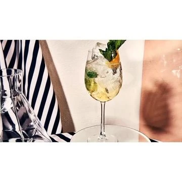 Refreshing spritzer cocktail with ice, mint, and orange peel served in elegant glassware against a striped backdrop.
