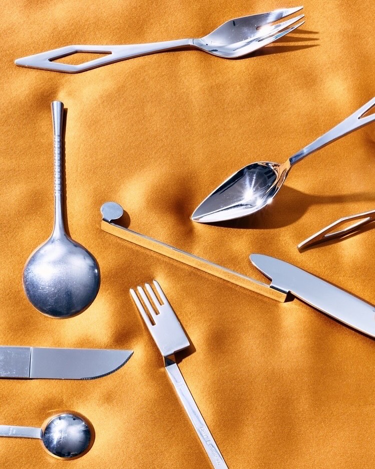Silverware arrangement on gold fabric. Includes forks, spoons, and knives in a studio setting, showcasing modern design and aesthetics.