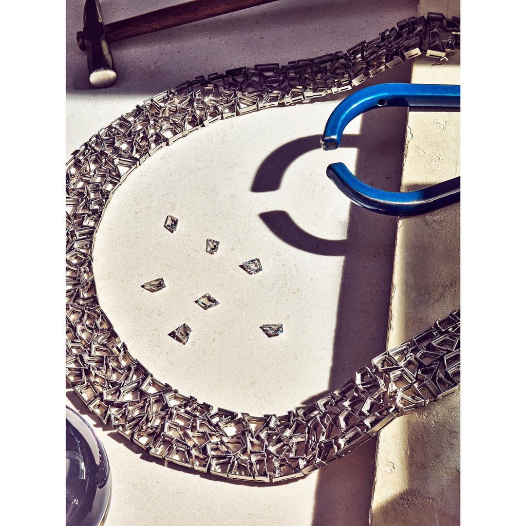 Abstract jewellery art featuring a chrome necklace with diamond-like accents and a blue object on a white surface with studio lighting.