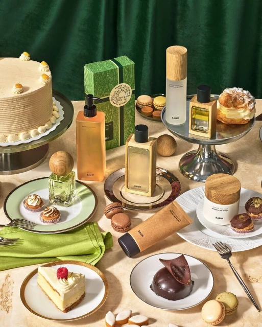 Luxury BAUM skincare products displayed alongside decadent desserts like cake, macarons, and chocolate mousse on an elegant table setting.