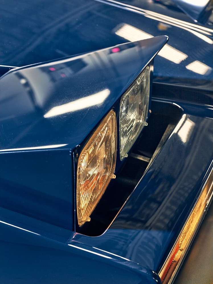 Close-up of a classic blue car headlight, showcasing its sharp design and reflective surface in bright light, automotive photography.