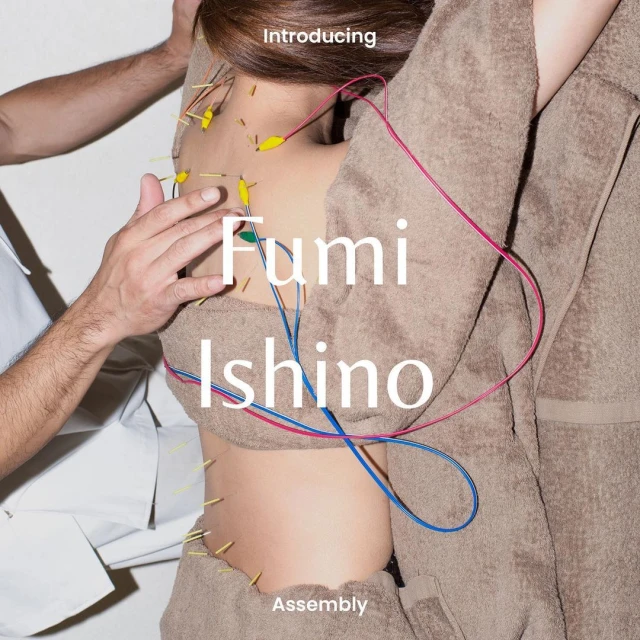 Close-up of a person's back and torso with multiple acupuncture needles, pink and blue cords, and another person's hands.
