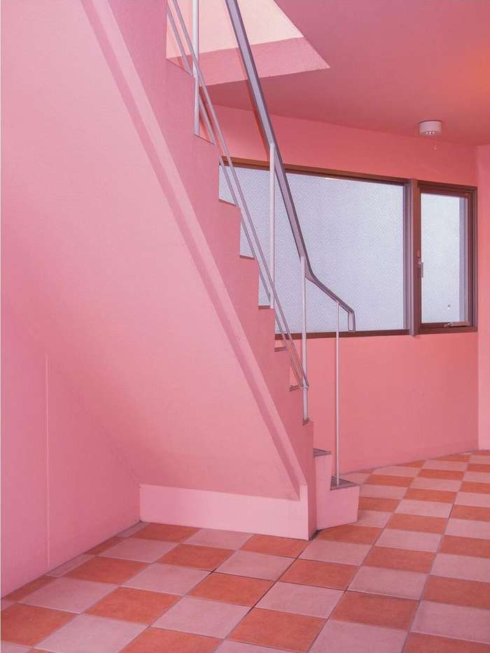 Minimalist interior with pink walls, checkered floor, and white staircase, creating a retro and modern aesthetic in a domestic setting.