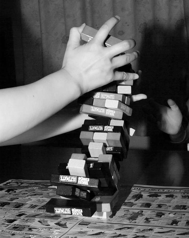 A stack of Jenga blocks is being manipulated by two players in a close-up shot, showcasing the game's tense moment on a detailed surface.