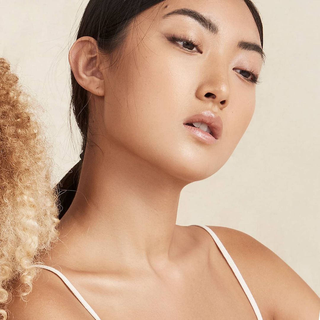 Close-up portrait of an Asian woman with fair skin and dark hair against a neutral background, highlighting beauty and skincare.