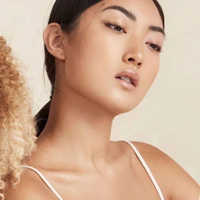Close-up portrait of an Asian woman with fair skin and dark hair against a neutral background, highlighting beauty and skincare.