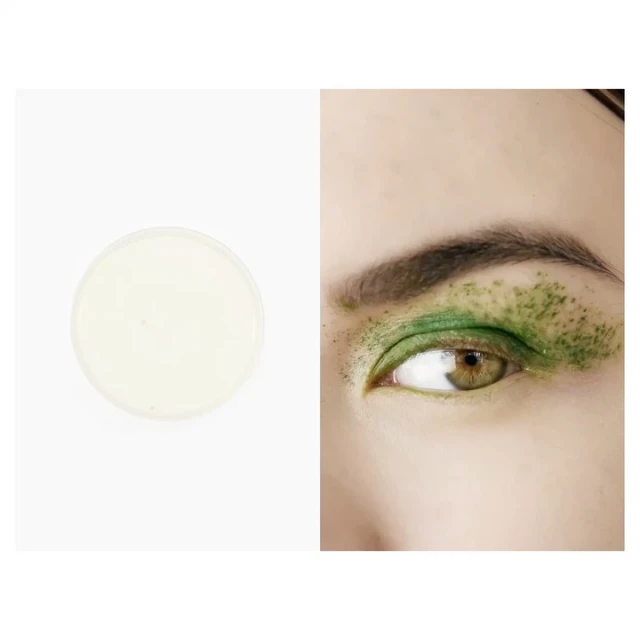 Close-up of a woman's eye with green glitter makeup alongside a container of white cream makeup on a white background.