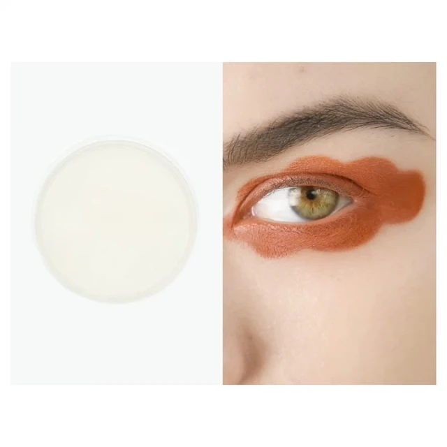 Close-up of a person's face showcasing creative orange eyeshadow in a cloud-like pattern, next to a skincare product on a white background.