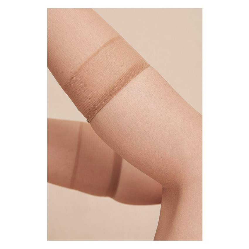 Close-up studio shot of an adult female's legs wearing sheer, nude-toned thigh-high stockings against a neutral backdrop.