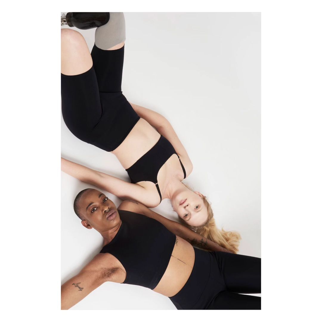 Two athletic women, one with a prosthetic leg, pose in black activewear on a white background. Active lifestyle fashion.