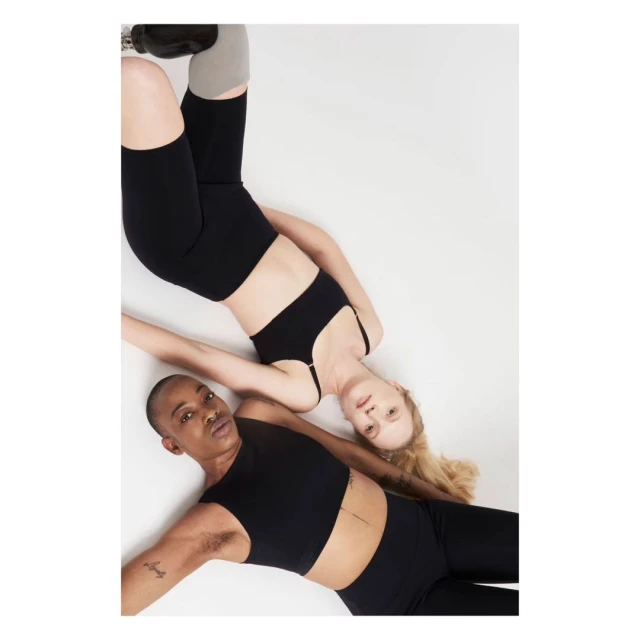Two athletic women, one with a prosthetic leg, pose in black activewear on a white background. Active lifestyle fashion.