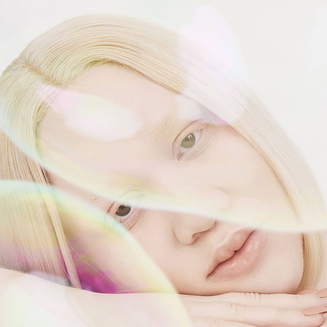 Portrait of a fair-skinned woman with albinism laying down, blonde hair, light eye makeup, with transparent bubbles in a light background.