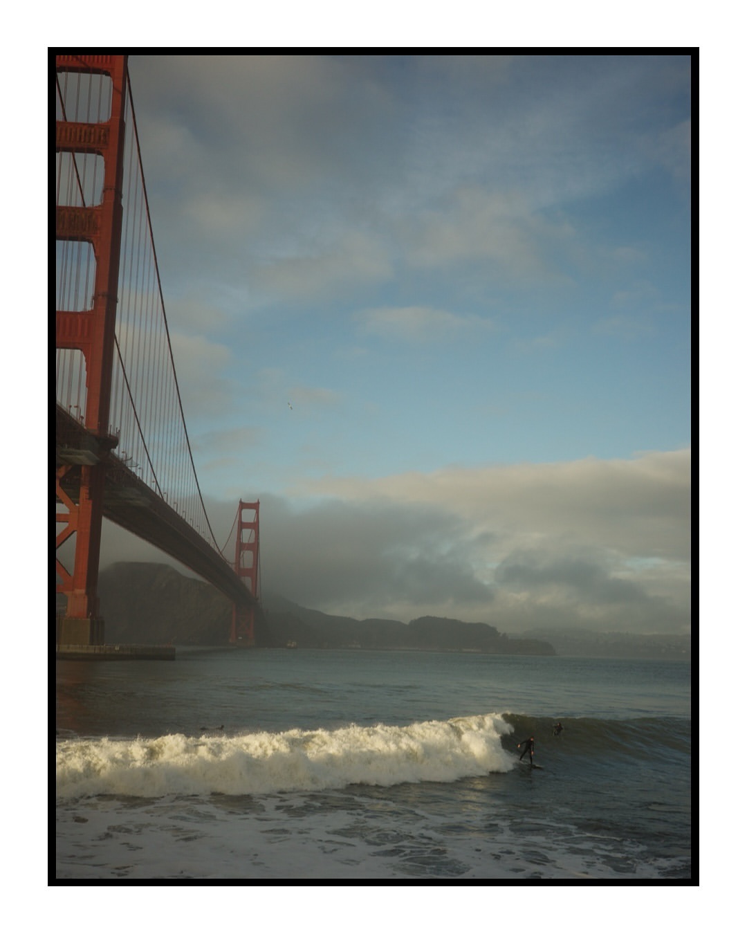 Golden Gate Bridge view with ocean waves and surfers, San Francisco, California, USA. A sunny day captures coastal scenery.