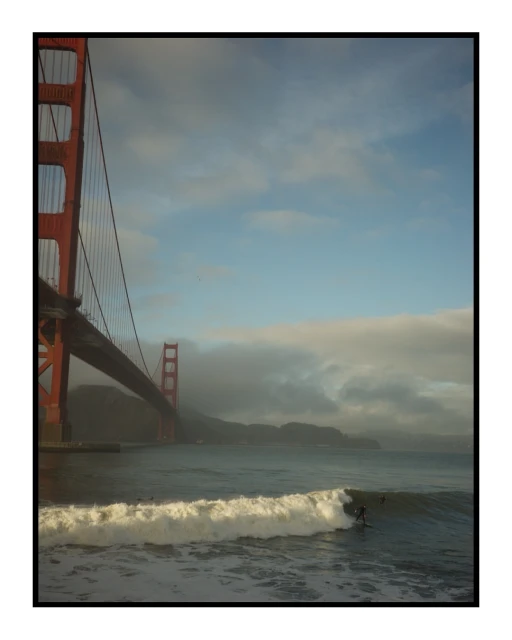 Golden Gate Bridge view with ocean waves and surfers, San Francisco, California, USA. A sunny day captures coastal scenery.