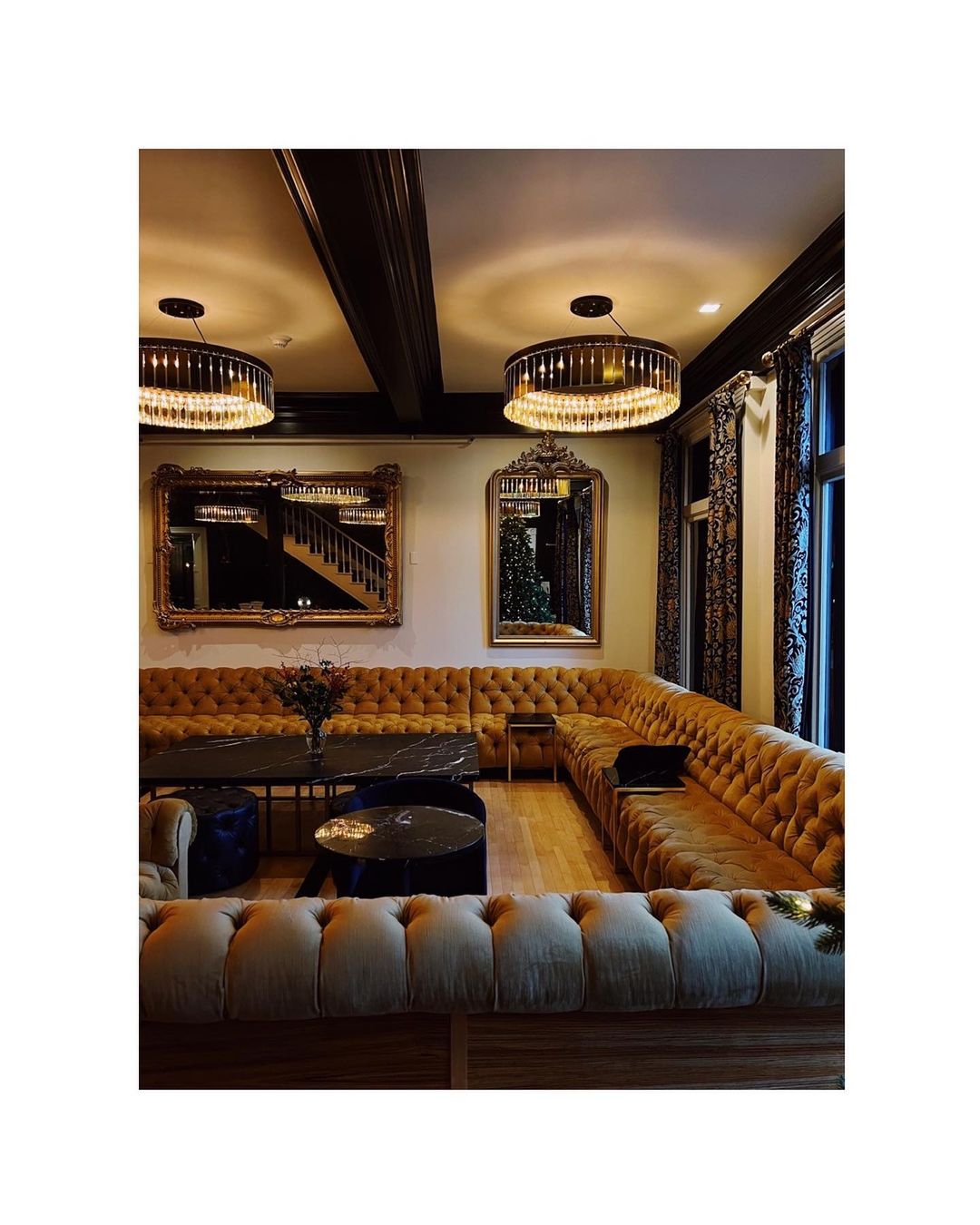 Luxurious lounge area features a U-shaped tufted couch, round coffee tables, elegant chandeliers, and ornate mirrors, creating a sophisticated space.