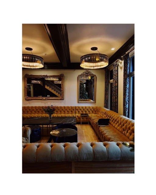 Luxurious lounge area features a U-shaped tufted couch, round coffee tables, elegant chandeliers, and ornate mirrors, creating a sophisticated space.