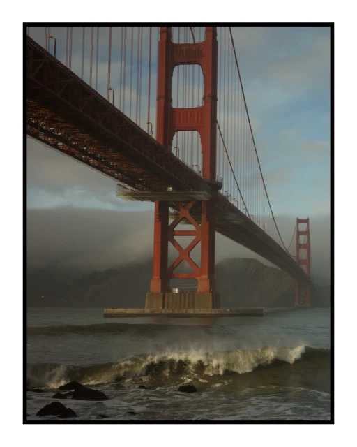 Golden Gate Bridge view from water level with ocean waves, fog, and cloudy sky, captured in a landscape orientation.