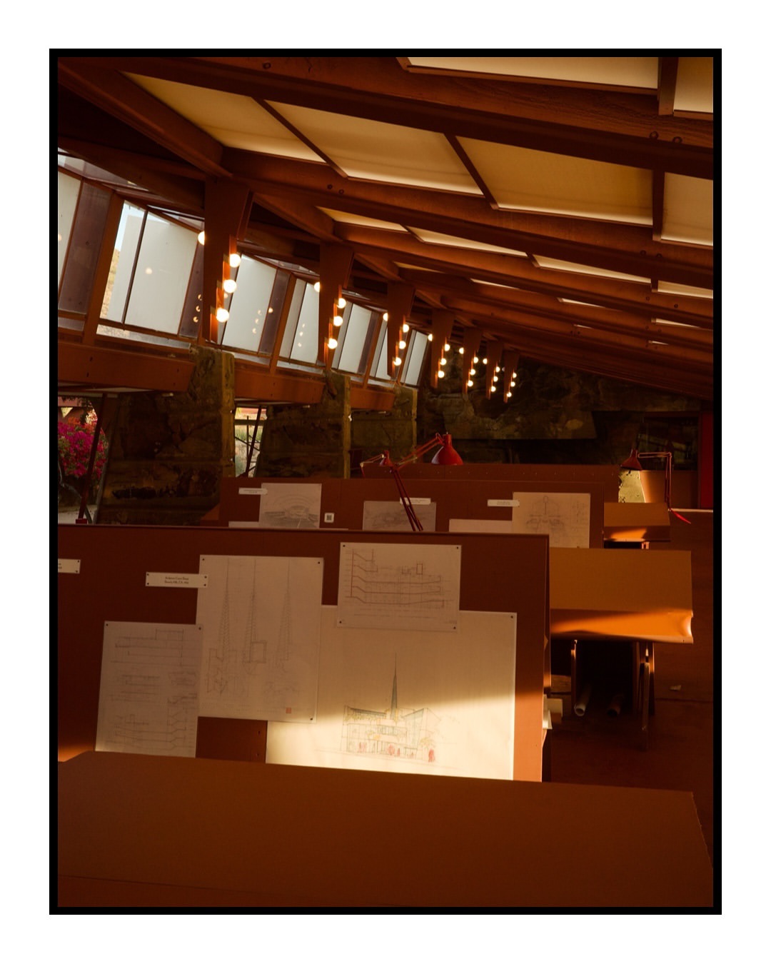 Interior view of an architecture studio featuring drafting tables with plans, soft natural lighting, and a high wooden beam ceiling.