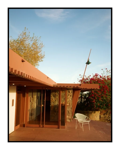 Exterior view of the iconic desert architecture of Taliesin West featuring a chair, red flowers, roofline, and blue sky.