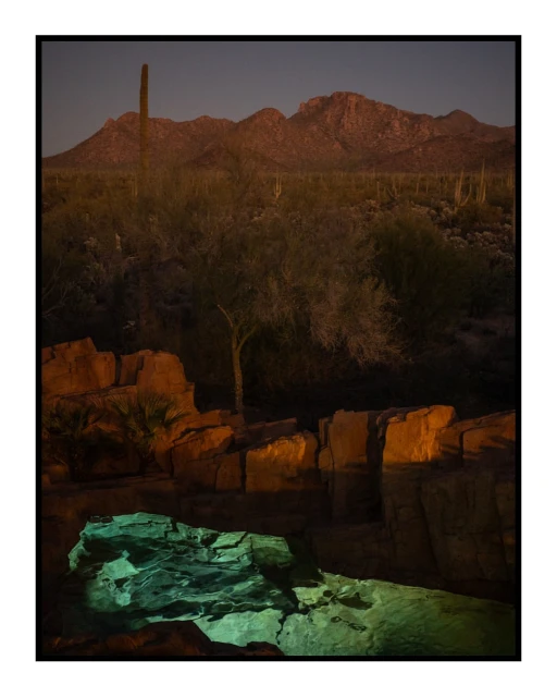 Desert landscape featuring rock formations, cacti, and mountains at dusk with striking turquoise rock in the foreground.