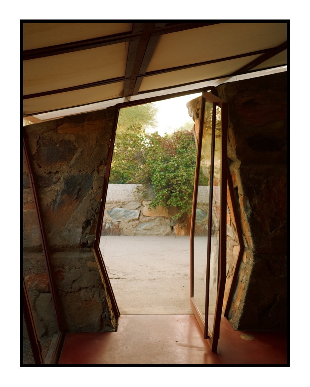 Architectural photo of a stone and metal structure, featuring a view to the outdoor garden with desert plants and a stone wall.