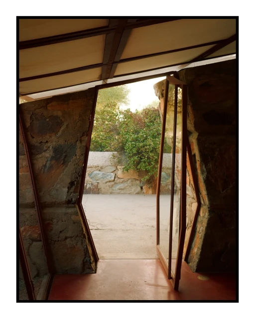 Architectural photo of a stone and metal structure, featuring a view to the outdoor garden with desert plants and a stone wall.