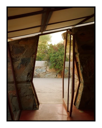 Architectural photo of a stone and metal structure, featuring a view to the outdoor garden with desert plants and a stone wall.