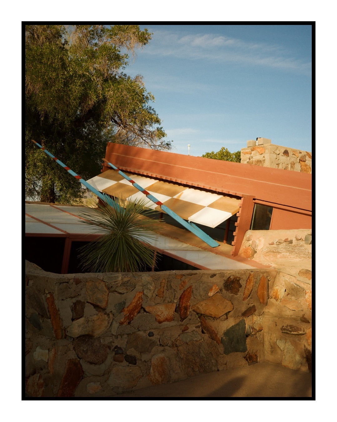 Architecture featuring a stone wall, geometric building with terracotta roof, and a blue and white structure in a desert environment.