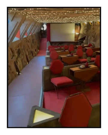 Interior view of a cozy home movie theater with red chairs and tables, featuring a projection screen and decorative ceiling lights.