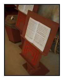 Two brown wooden music stands with sheet music open, standing on a carpeted floor in a room interior.
