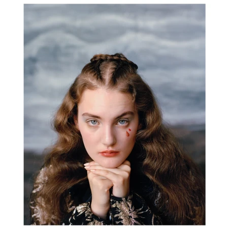 Portrait of a young woman with auburn hair and a braided crown, resting her chin on her clasped hands. A single red tear marks her cheek.