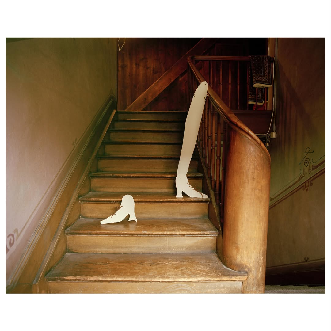 Whimsical art photo of abandoned white shoe forms on wooden stairs with dark wood banister in a traditional residential building.