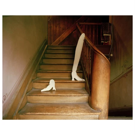 Whimsical art photo of abandoned white shoe forms on wooden stairs with dark wood banister in a traditional residential building.