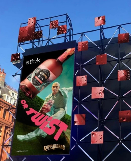 Advertisement for Kopparberg Gin featuring a man holding a bottle in front of a green hedge, displayed on a large billboard.
