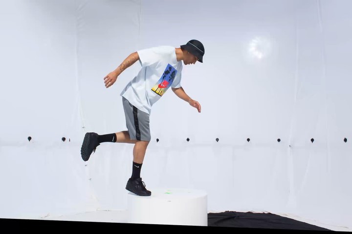 Man in casualwear jumps off platform in studio setting.  He wears a tee shirt, shorts, bucket hat, and sneakers, poised mid-air.