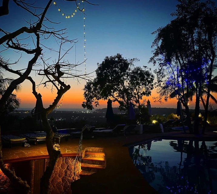 Tranquil twilight scene of a terrace with pool, trees, and a distant cityscape under an orange and blue gradient sky.