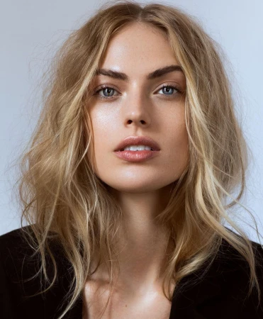 Close-up portrait of a woman with blonde hair, blue eyes, and natural makeup against a plain background