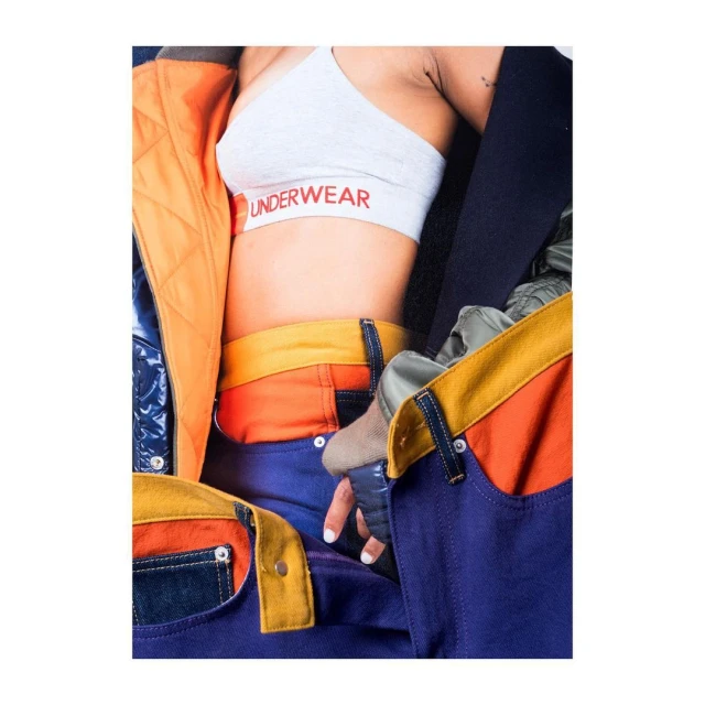 Close-up studio shot of a person wearing a grey sports bra with 'UNDERWEAR' printed on it and blue jeans with yellow accents.