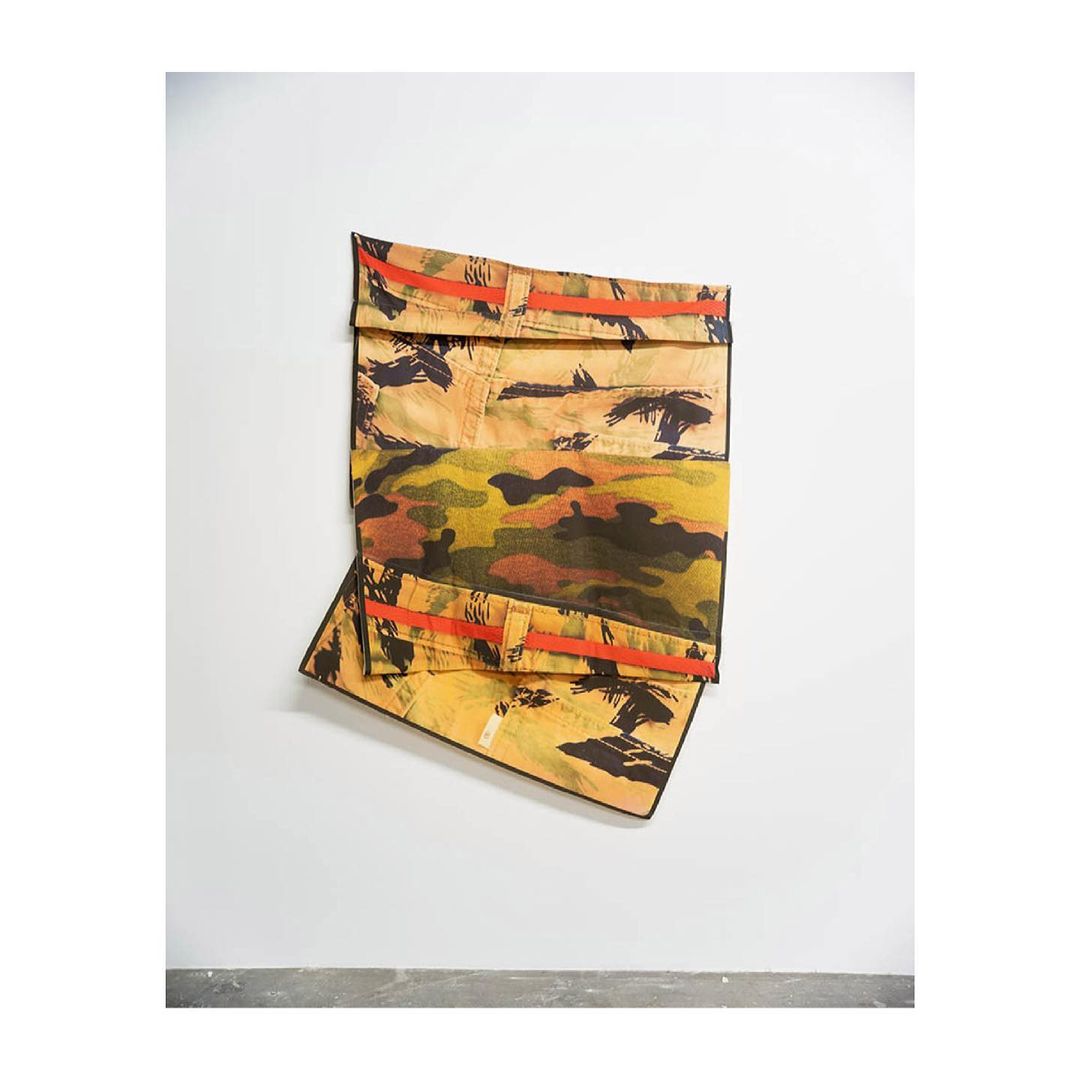 Abstract photograph of camouflage-patterned textile art hanging on a white wall, with a focus on colors, textures, and design.