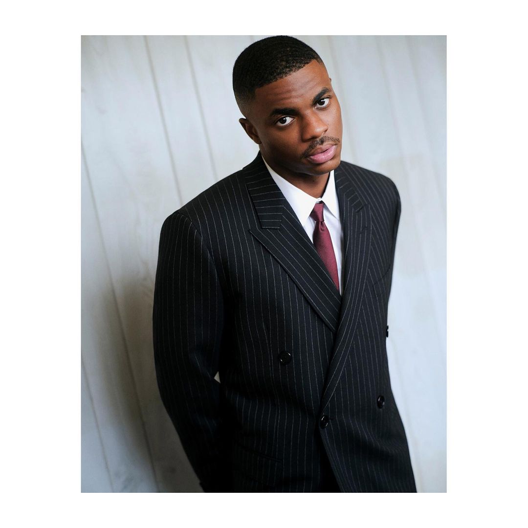 Portrait of an African-American adult male in a pinstripe suit and maroon tie looking at the camera against a textured backdrop.
