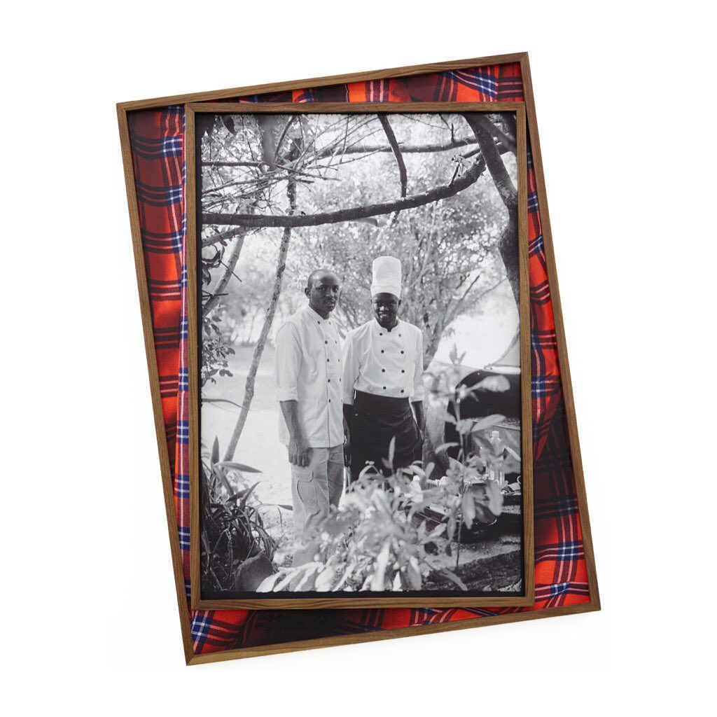 Framed black and white photograph of two men, one wearing a chef's hat, framed in a wooden frame with a red, blue, and white plaid fabric.