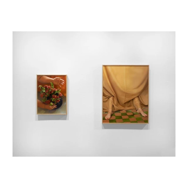 Two framed fine art photographs on a white wall: roses in a vase and a person draped in fabric with checkerboard floor beneath.