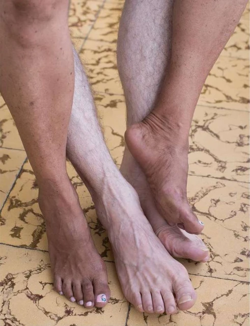 Close-up of two people's legs and feet, one fair-skinned and one brown-skinned, standing on a tile floor, showcasing diversity.