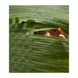 Close-up portrait of a person peering through a woven green banana leaf structure